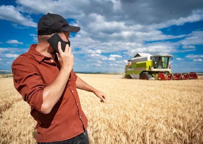 mężczyzna na polu przed maszyną rolną rozmawiający przez telefon